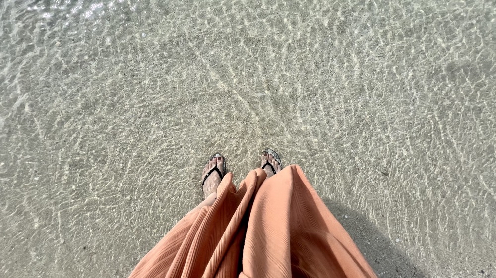透明度の高い海の浅瀬に入っている足元と涼しげなスカートを写した風景