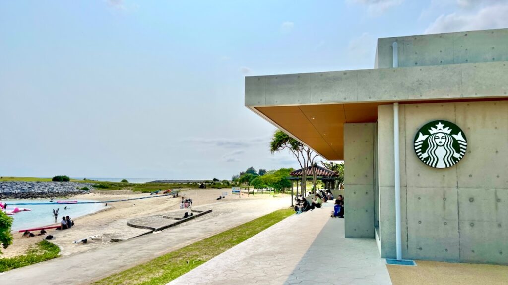 名護21世紀の森公園のビーチ沿いに佇むスターバックスの外観。エメラルドグリーンの海とコンクリート打ち放しのモダンな建物。