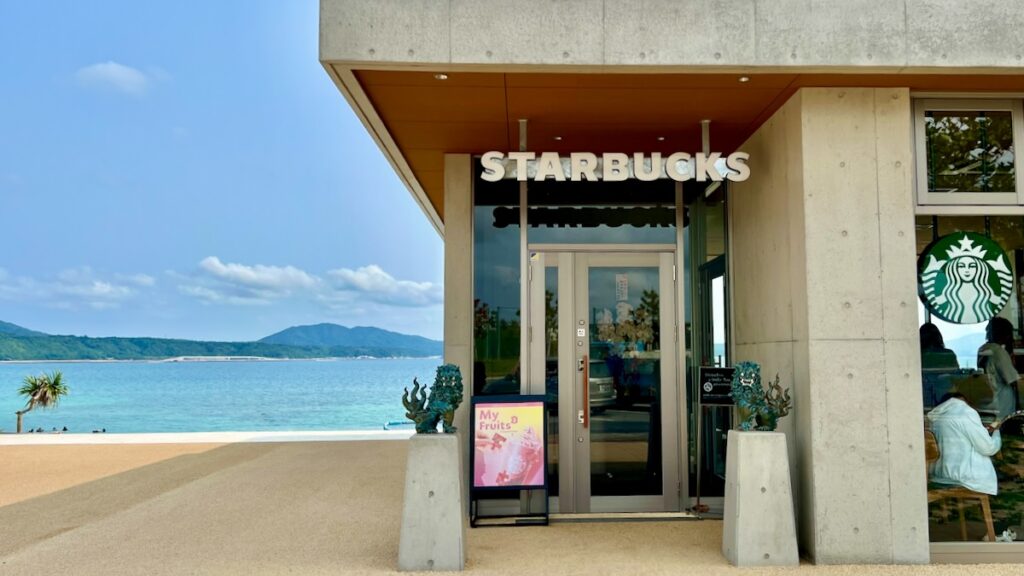 店舗入り口で出迎える沖縄伝統のシーサーと、背景に広がる名護の青い海。