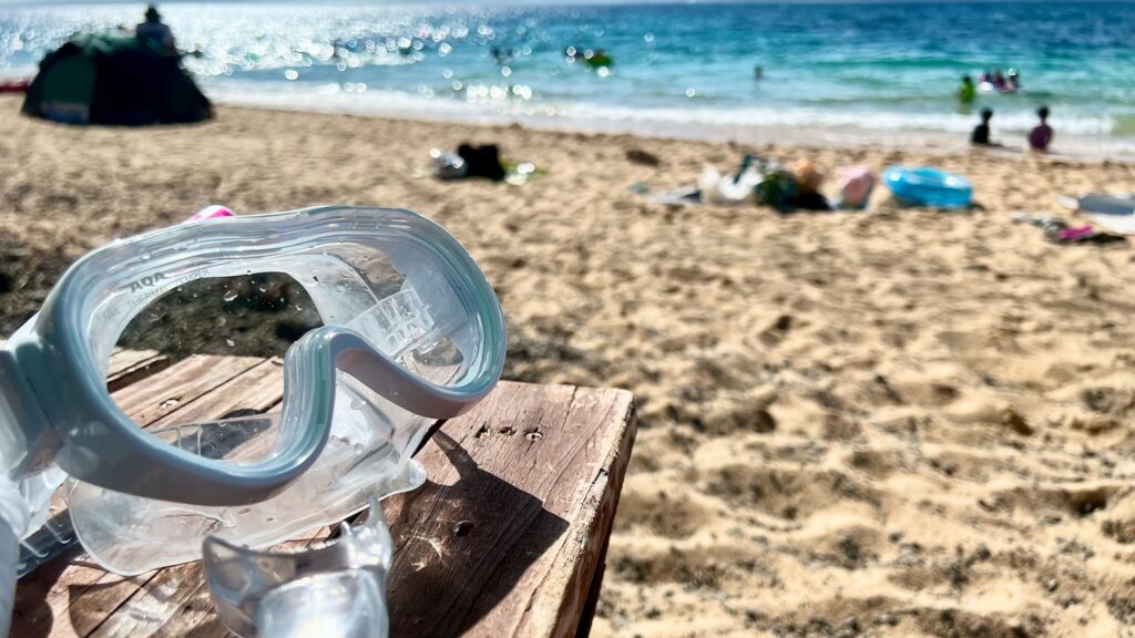 海と白い砂浜を背景に、テーブルの上にシュノーケルマスクがある大泊ビーチの風景