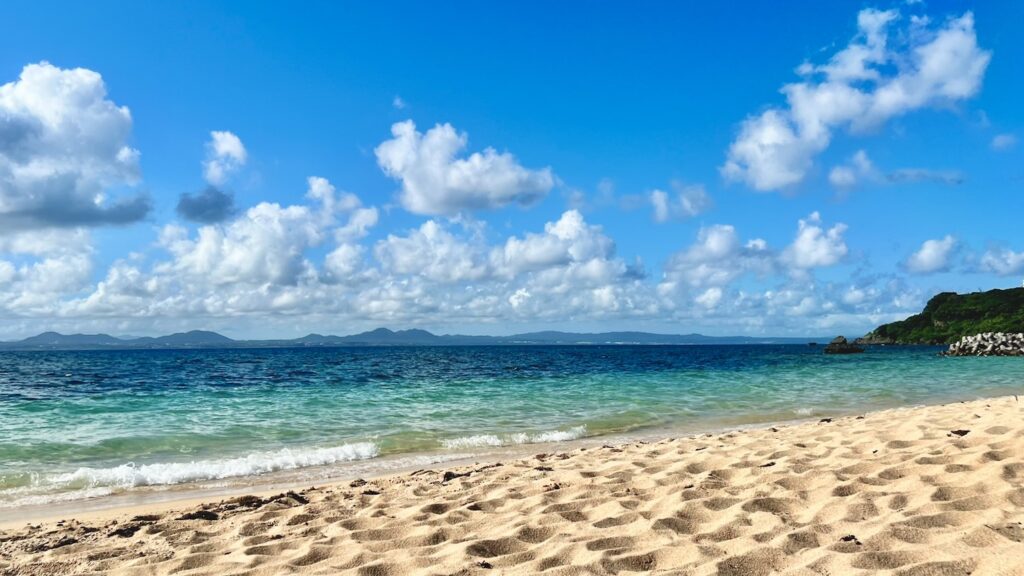 青空と雲が広がる空の下に、エメラルドグリーンの海と白い砂浜が広がる大泊ビーチの波打ち際