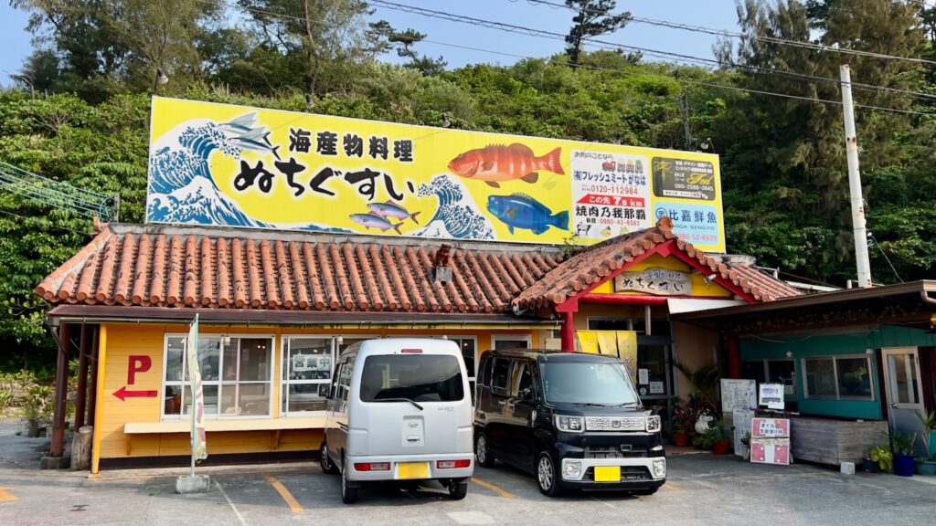 黄色基調の建物に赤い屋根と魚の看板が印象的な食堂「海産物料理ぬちぐすい」の外観