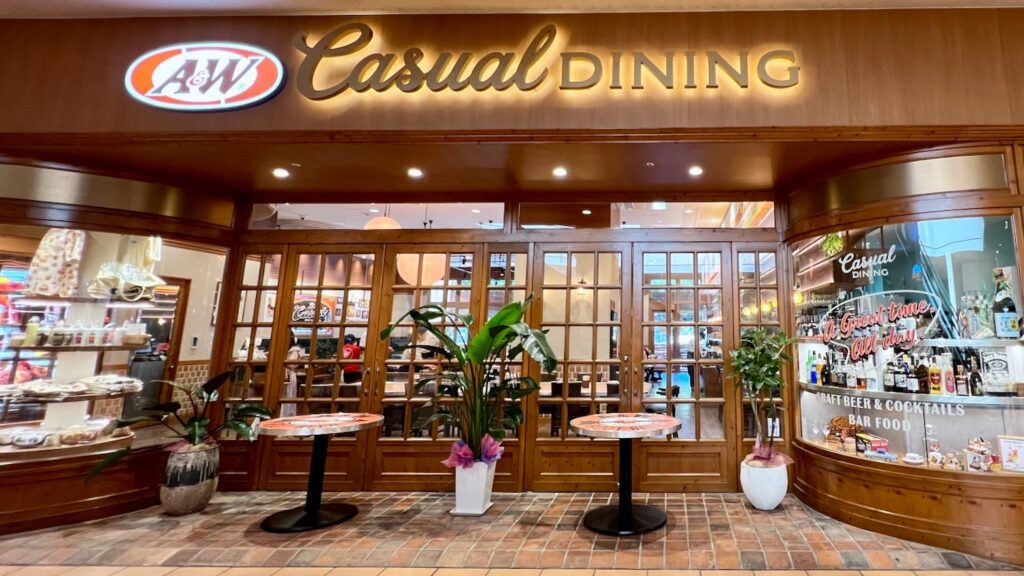 グッズやお酒が綺麗にレイアウトされた様子と店内が見えるA&W casual diningの木目調の店舗外観と入り口