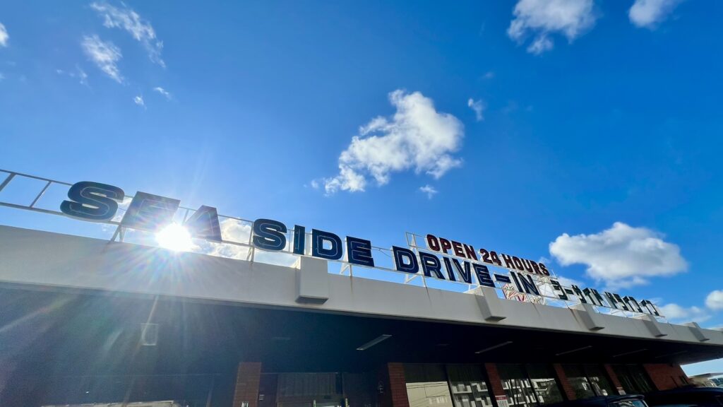 太陽と青空を背景にした、「SEA SIDE DRIVE - IN シーサイドドライブイン」の文字があるレトロな看板