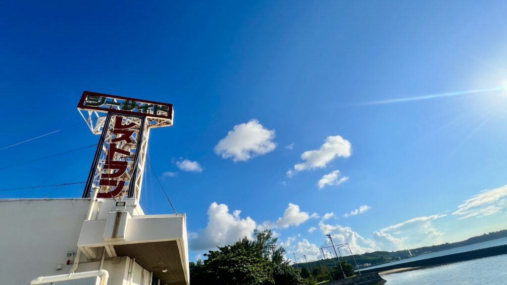 青空と海を背景にした、「シーサイド レストラン」の文字があるレトロな看板