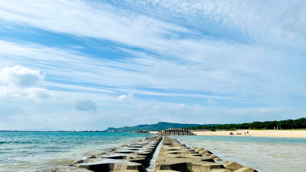 沖縄のビーチで海へと真っ直ぐ伸びるコンクリート製の離岸堤。コバルトブルーの海と筋状の雲が広がる空の絶景。