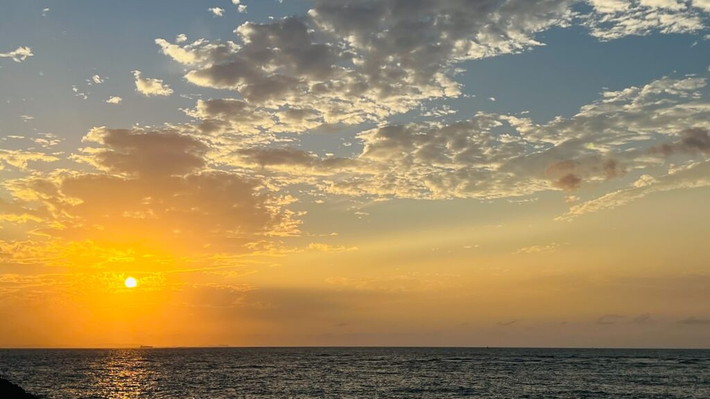 沖縄の海に沈む黄金色のサンセットと、夕焼け空に広がる美しい雲の風景