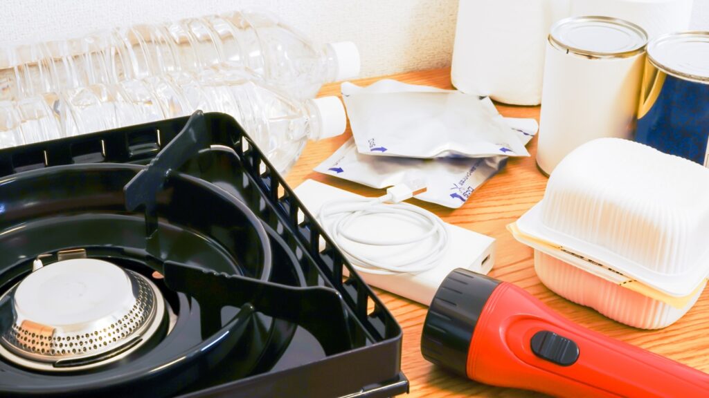 水、モバイルバッテリー、懐中電灯、カセットコンロ、レトルト食品が並んでいる画像