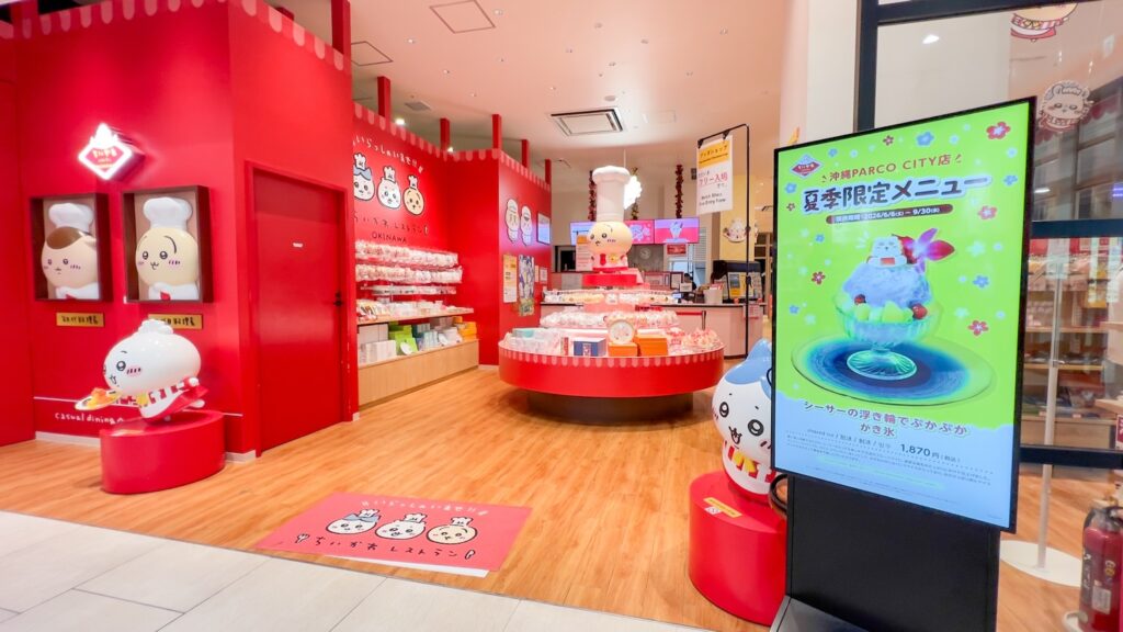ちいかわレストランの入り口から見た、赤を基調にした店内とウェイターやシェフの衣装を着たちいかわ達のかわいいモニュメントがある風景