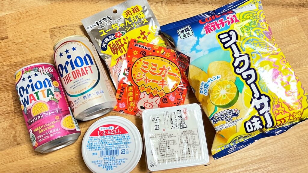 テーブルにオリオンビール、WATTA、ジーマーミ豆腐2つ、ポテトチップス、砂肝ジャーキー、ミミガージャーキーが並んでいる画像。