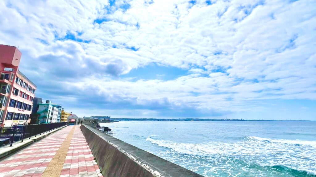 左側にカラフルなビルが立ち並び、右側に青い海が広がる宮城海岸の遊歩道の風景