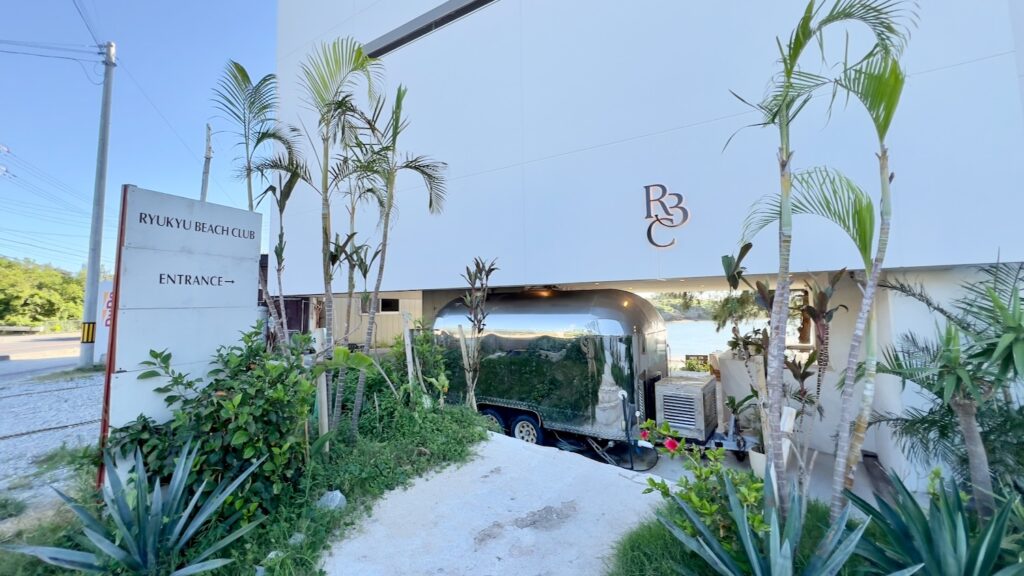 RYUKYU BEACH CLUBの白いおしゃれな外観と植物の緑が綺麗なエントランスの風景