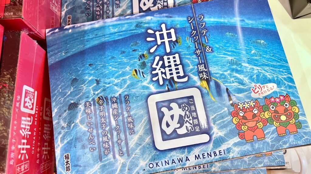透明な水の中にカラフルな魚が泳いでいる写真とシーサーのイラストが描かれている「沖縄めんべい ラフテー＆シークヮーサー風味」のパッケージ